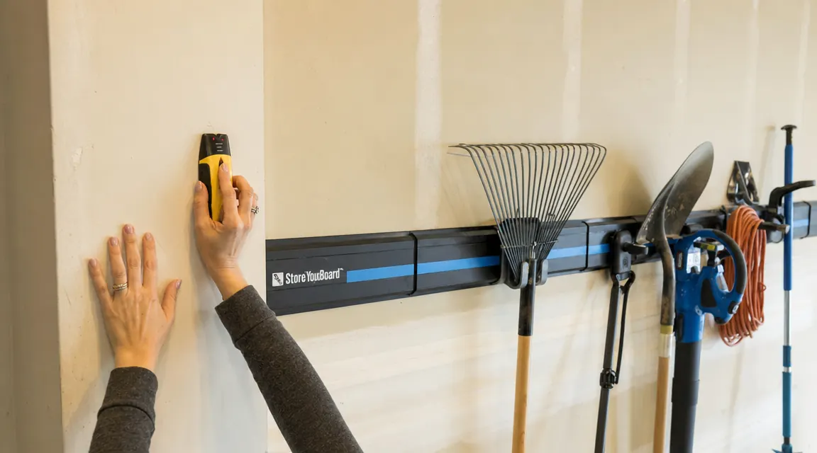 Hand pressing a stud finder against a drywall garage wall, finding stud position before drilling